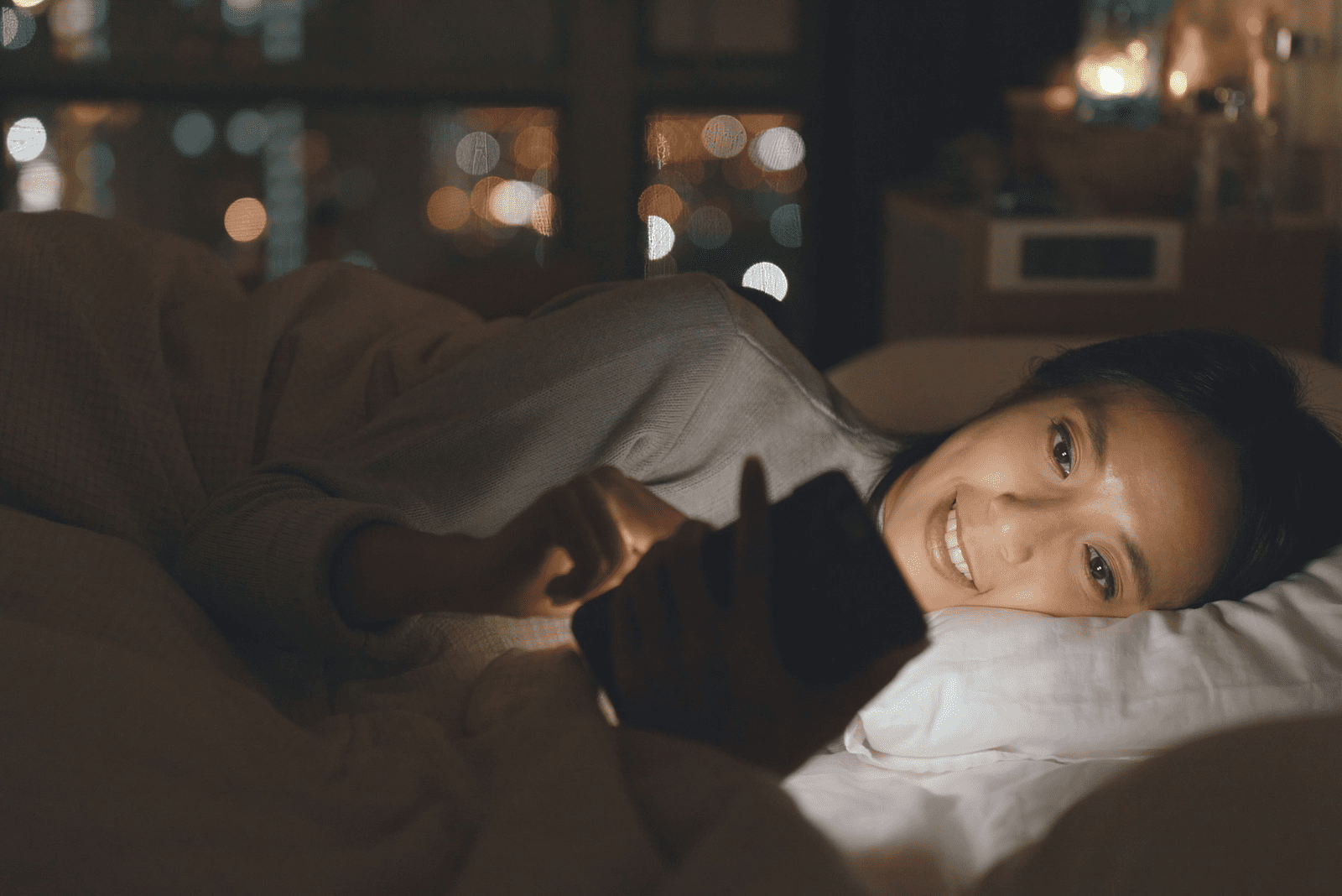 une femme est allongée dans son lit et regarde le téléphone
