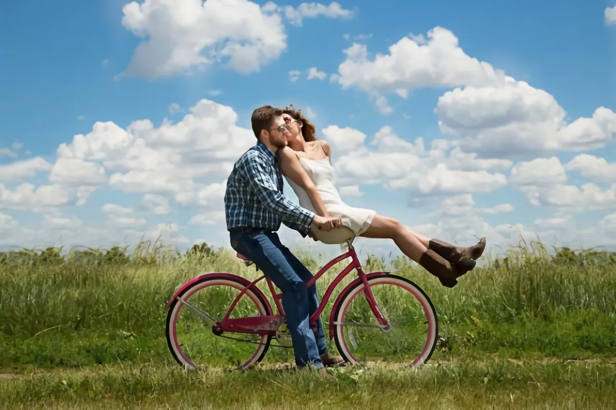 a happy couple on a bicycle in a field on a background of blue sky with some white clouds