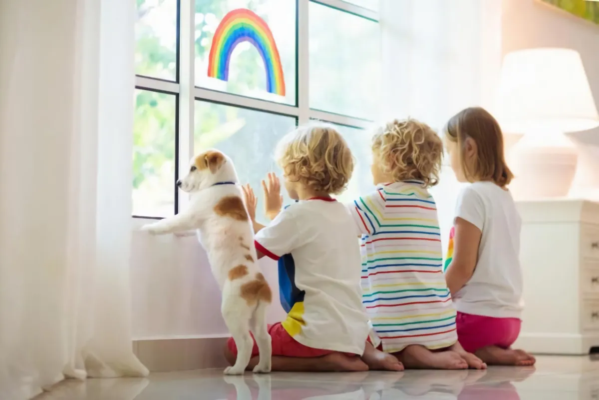 three children with a small dog look out the window sitting on a shiny floor in a white interior